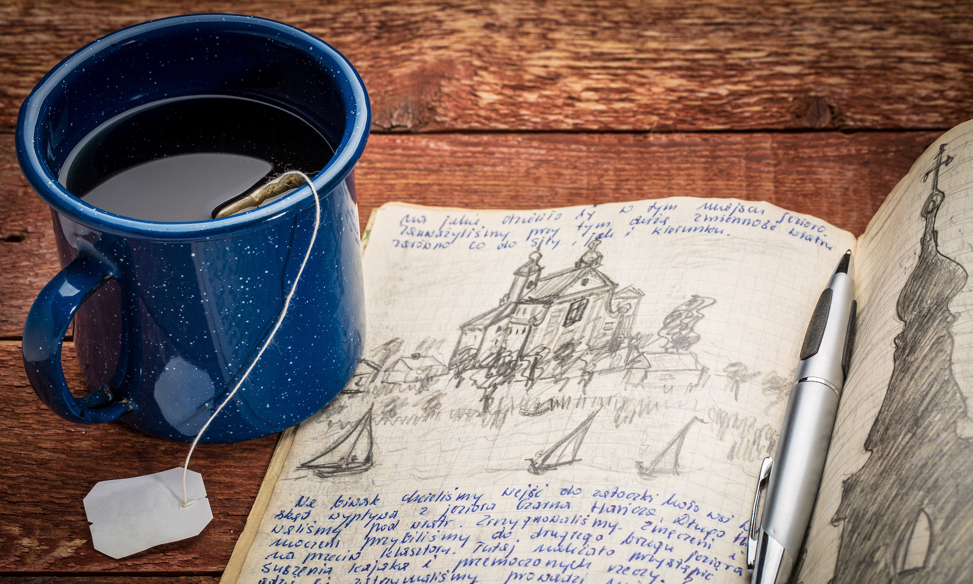 journal with handwriting and drawing in pencil in a notebook against rustic picnic table with cup of tea