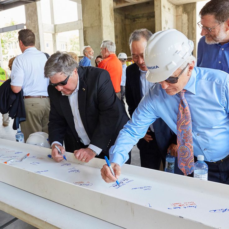 men wearing glasses and hard hats sign a beam