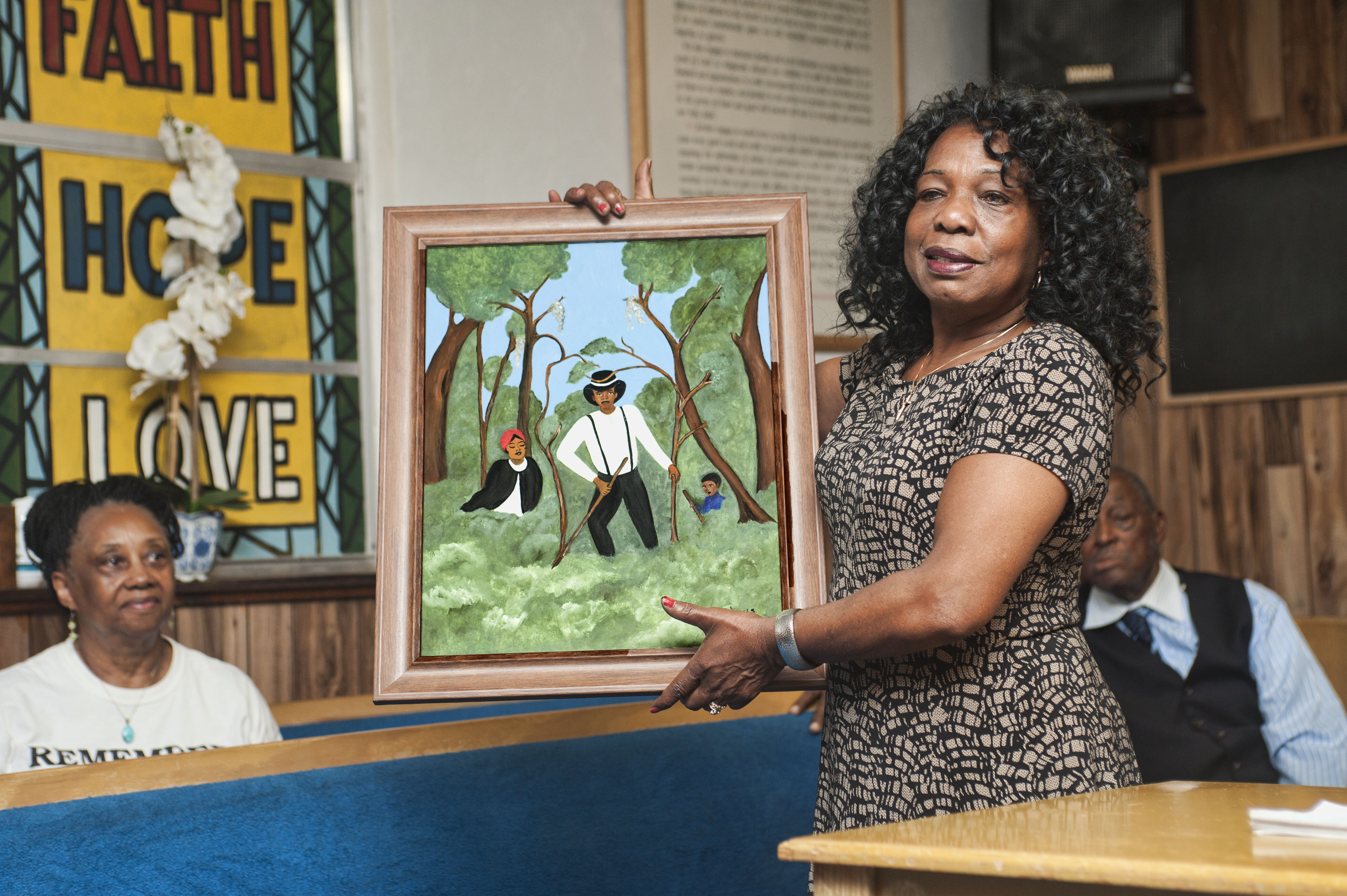 The summer program includes a trip to Rosewood, Fla., where students learn about the 1923 massacre of its black citizens. The photo shows an African American woman holding a painting of a small family hiding in the woods around Rosewood.