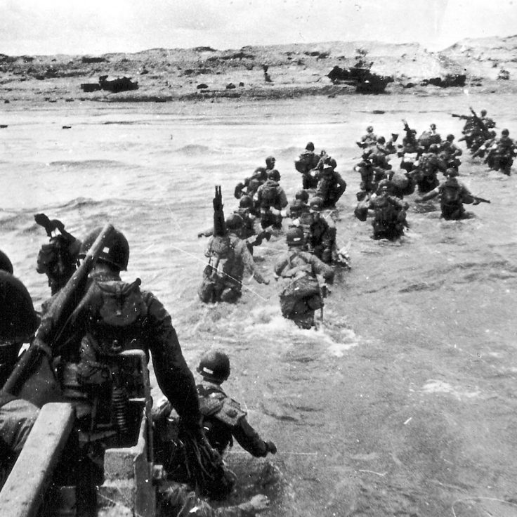 soldiers wade out of sea onto Normandy Beach