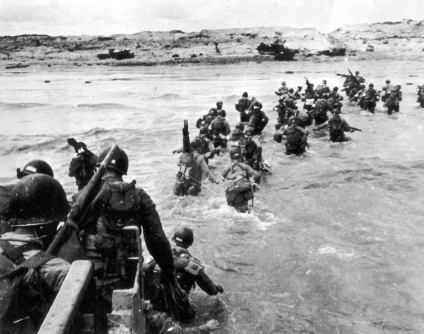 soldiers wade out of sea onto Normandy Beach