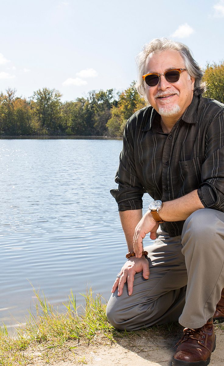 Photo of Tom Bianchi kneeling next to Lake Alice.