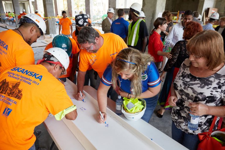 men in hard hats and two women sign the beam