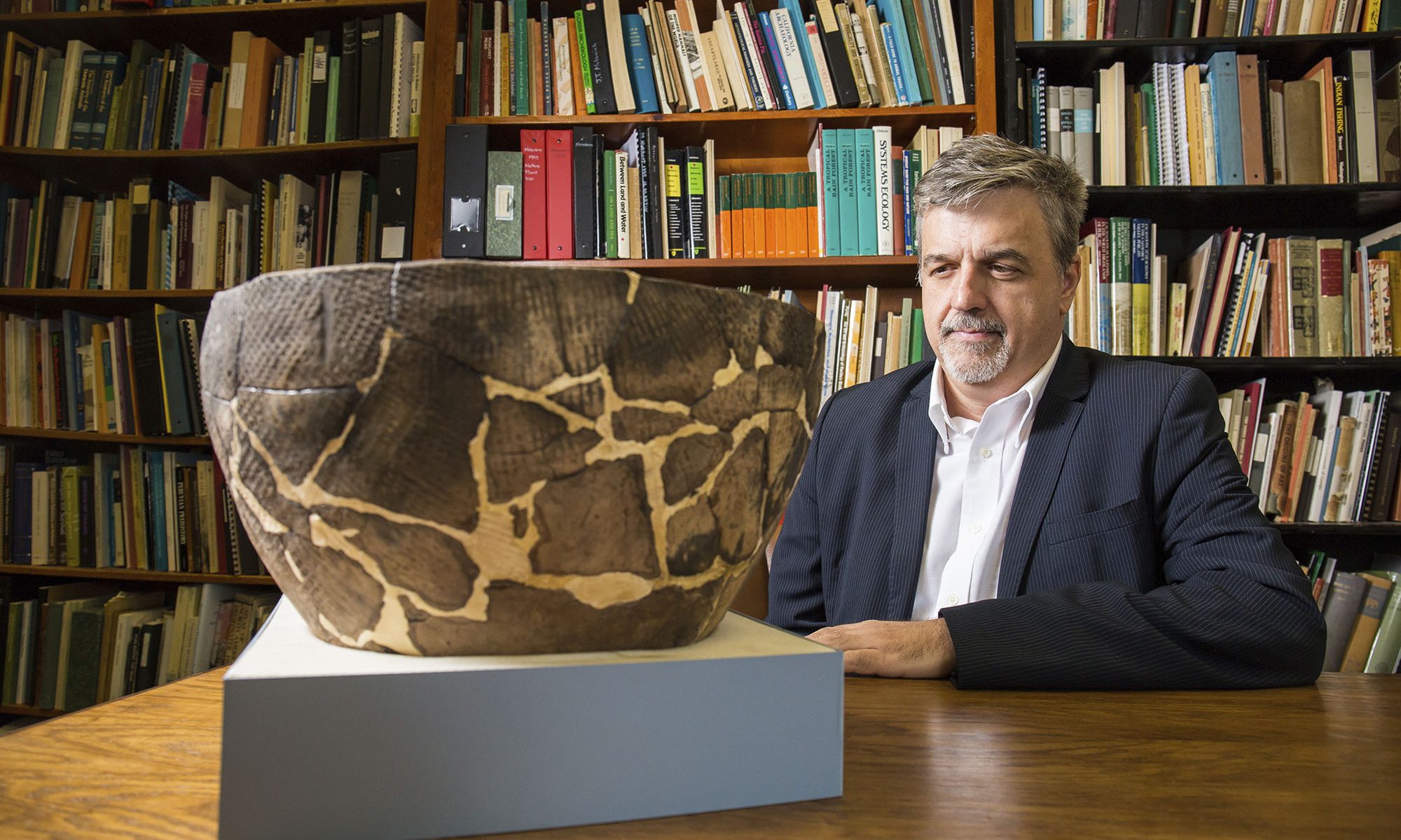 Aaron Broadwell sits in study with large artifact on table in front of him
