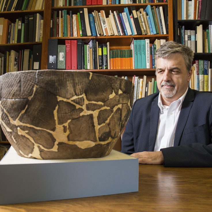 Aaron Broadwell sits in study with large artifact on table in front of him