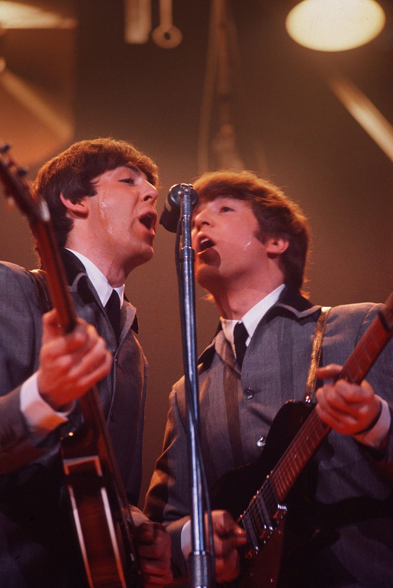 Paul McCartney and John Lennon singing at mic and holding guitars