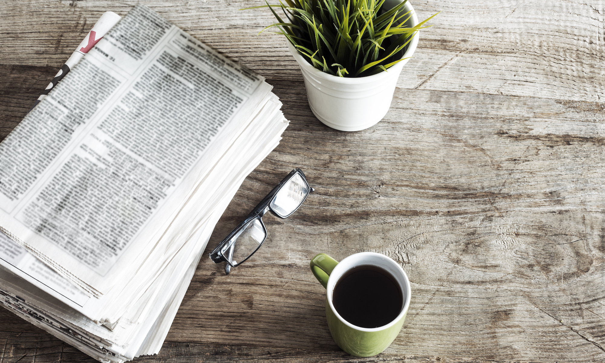 newspaper, plant, reading glasses, and coffee on wooden table