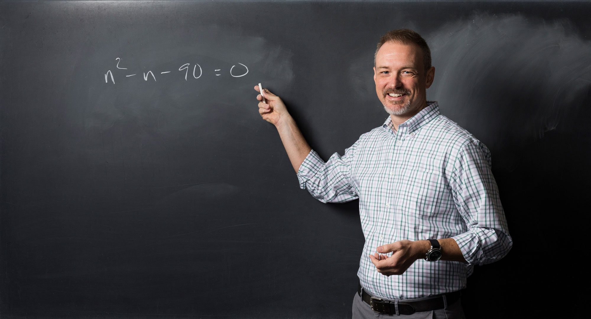 Kevin Knudson points to math equation written on chalkboard