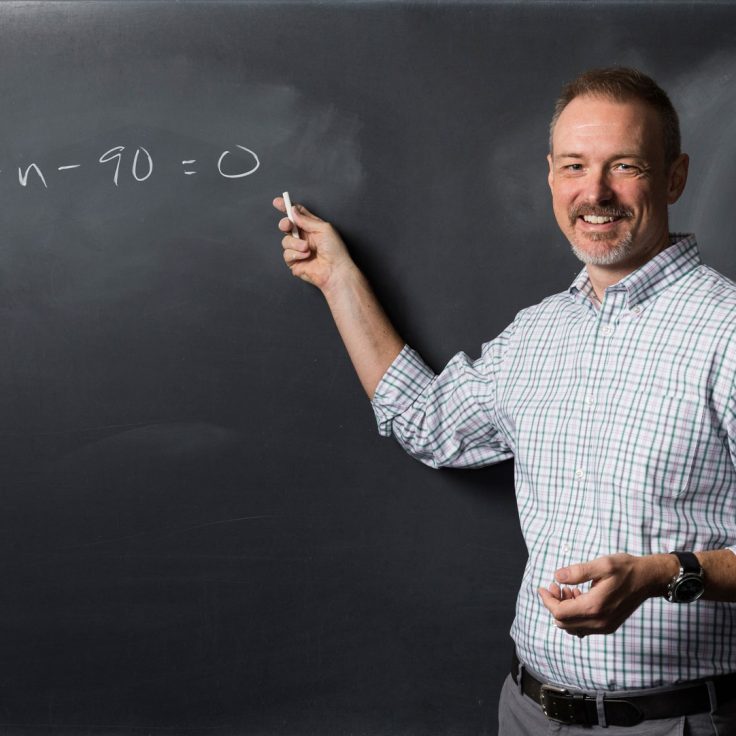 Kevin Knudson points to math equation written on chalkboard