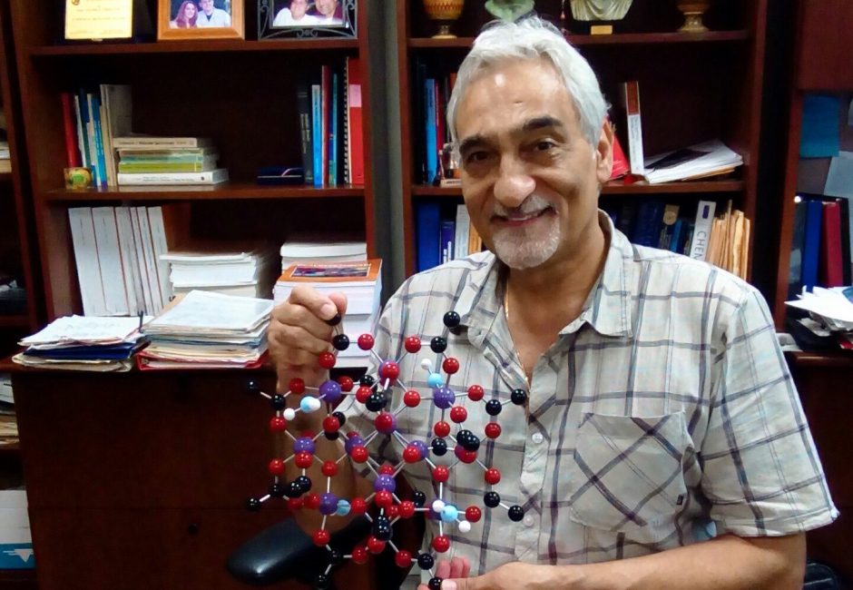 man holding molecular model sitting in front of bookshelf