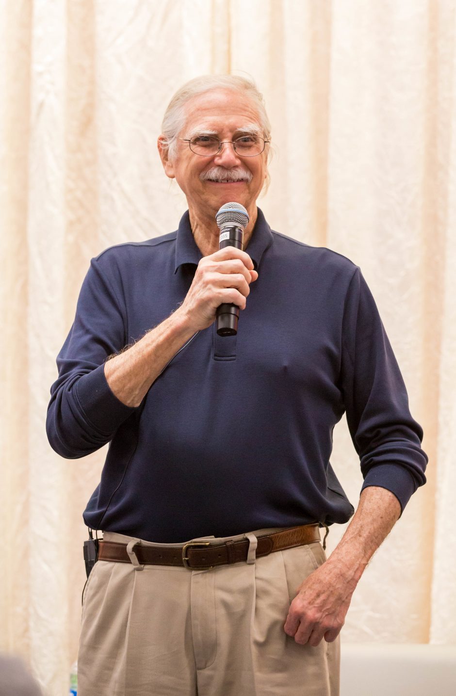 friendly older man holds mic while smiling