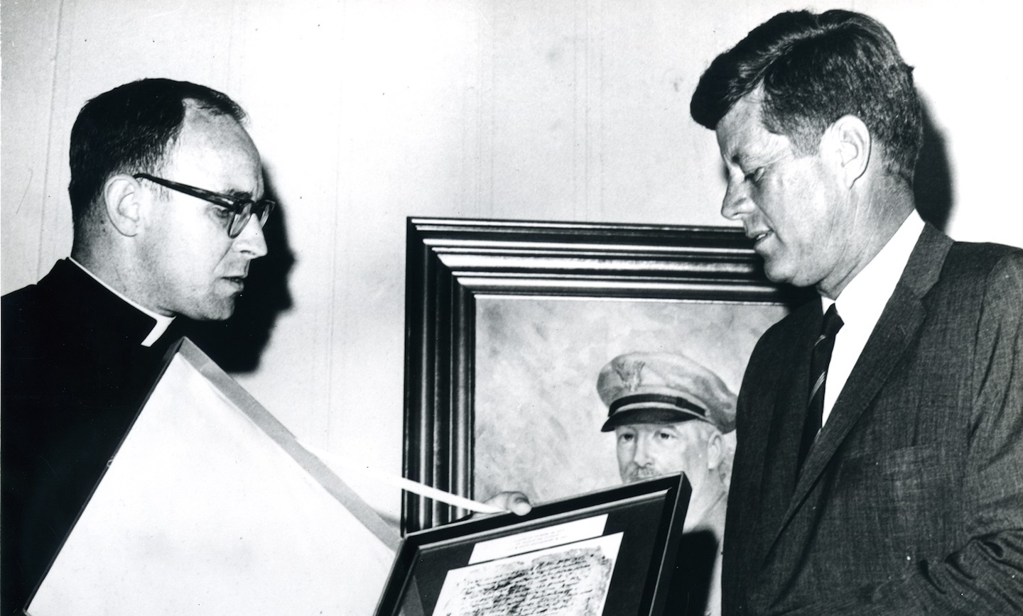 black and white photo of Gannon with JFK looking at old book