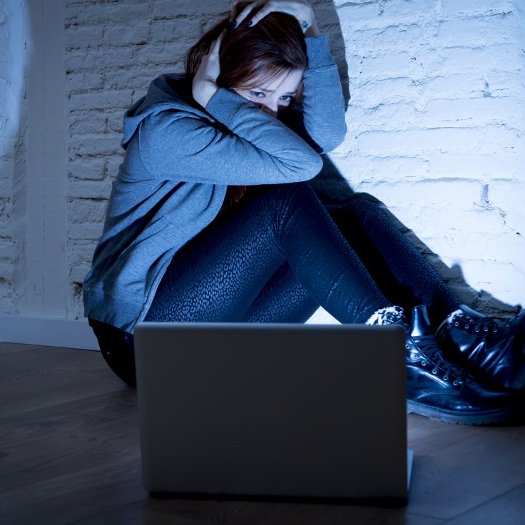 sad and scared female teenager with computer laptop suffering cyberbullying and harassment being online abused by stalker or gossip feeling desperate and humiliated in cyber bullying concept