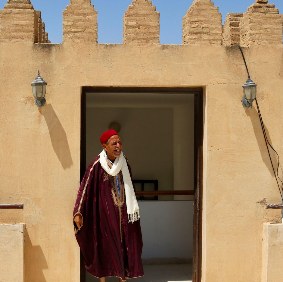 grinning man in traditional attire exits doorway of mosque