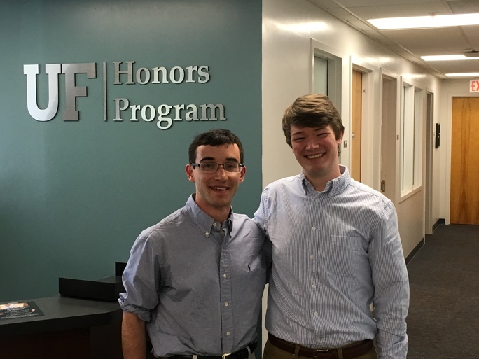 photo of two smiling young men standing in front of green wall with insigna reading "Honors Program"