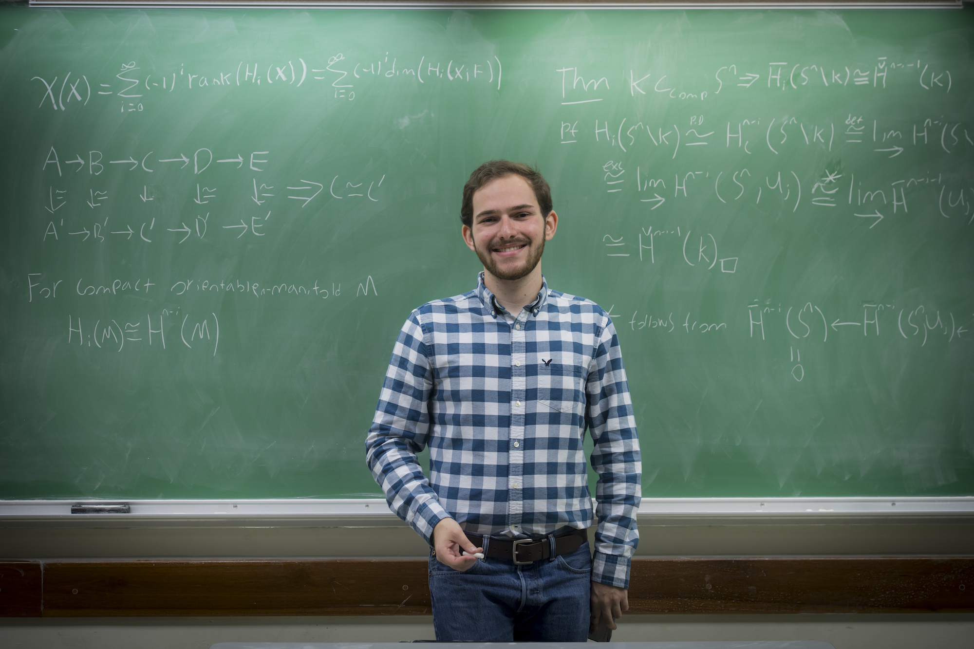 young man standing in front of green chalkboard with math equations