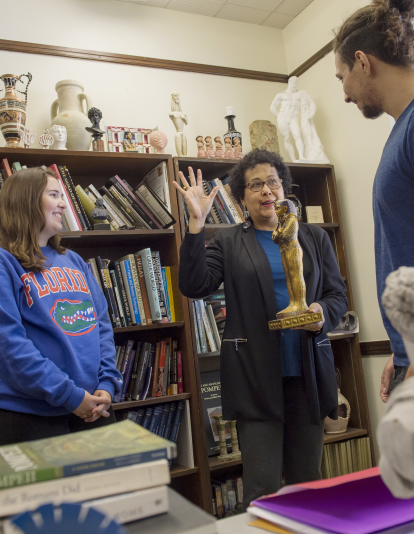 two students excitedly engage with Mary Ann Eaverly, who is holding an Egyptian statue