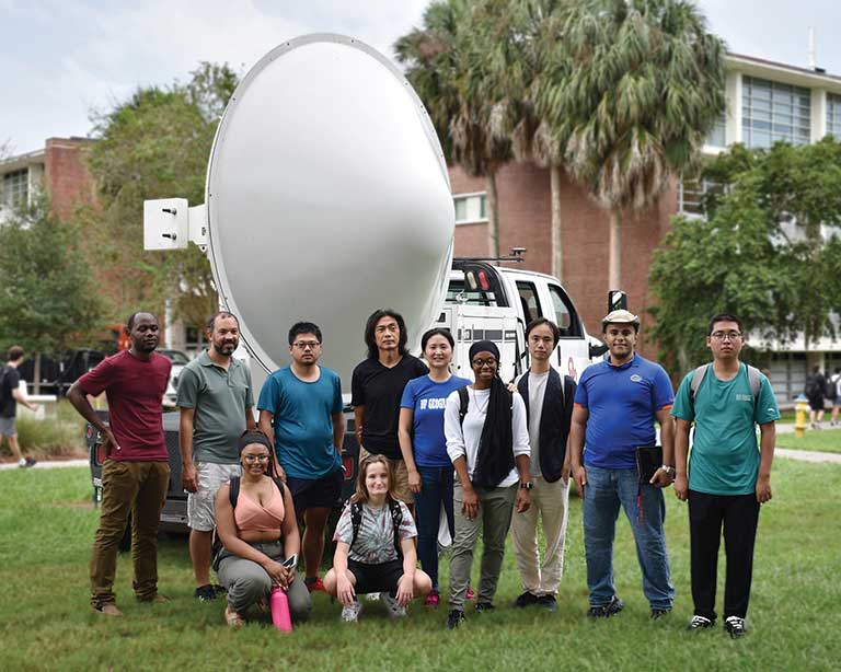 A team of researchers stand in front of the mobile radar unit on UF's campus.