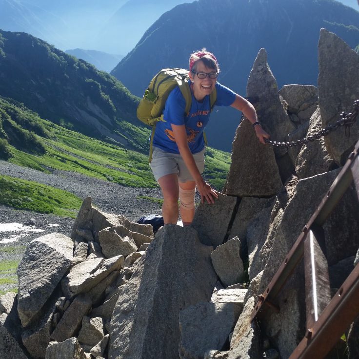 Marta Wayne hikes on top jagged rocks in Japan with mountains in background.
