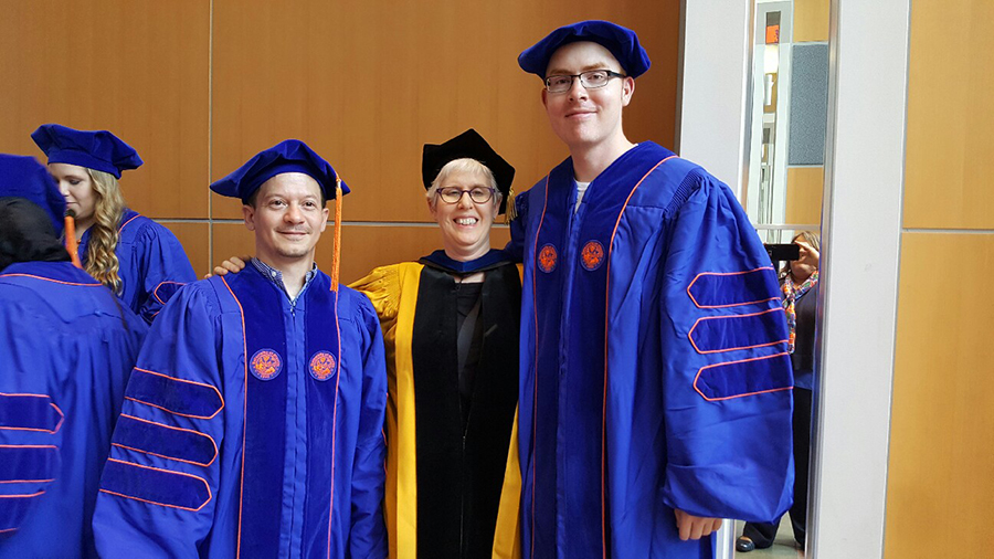 Dr. Shifra Armon stands between two graduating students, all wearing their respective ceremony attire