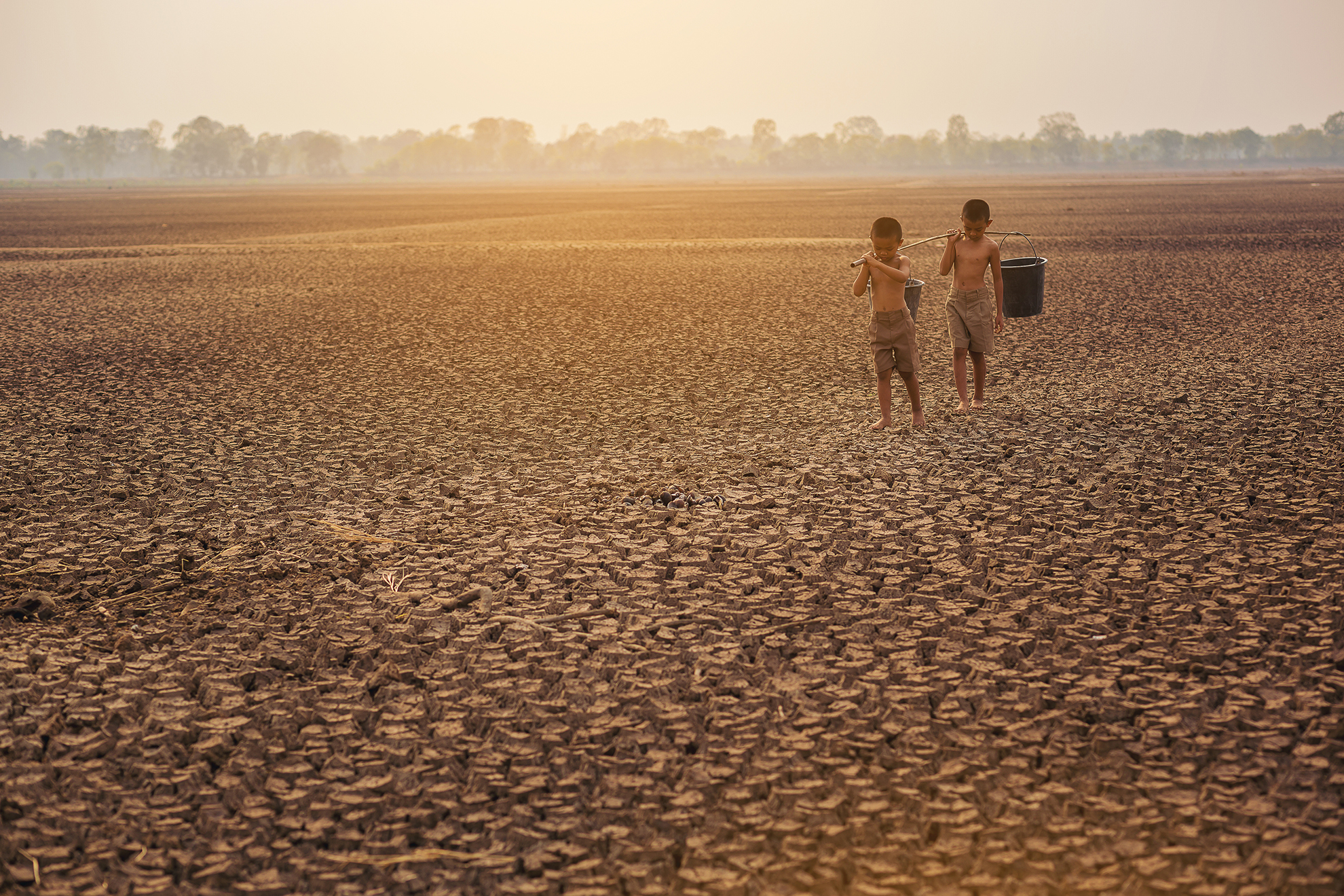 Two boys cross a parched landscape with buckets of water