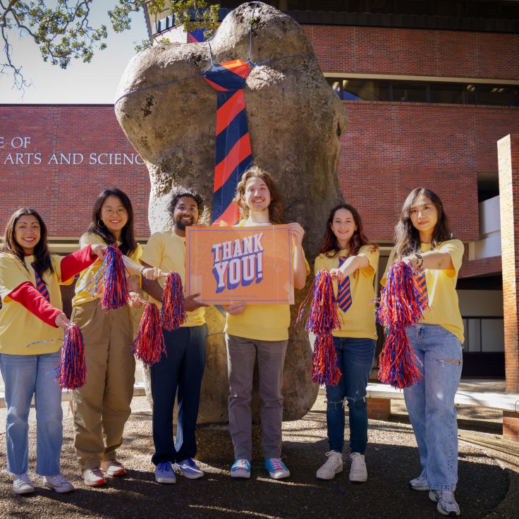 Five students dressed in yellow and the iconic Two Bits tie hold a "Thank You" sign in front of the Turlington rock.