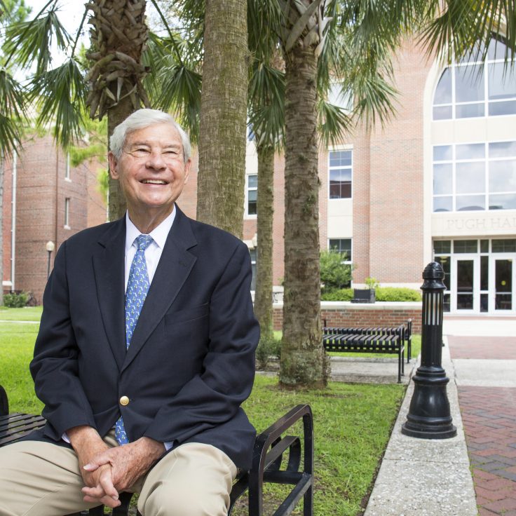 Bob Graham sits on a bench in front of a campus building
