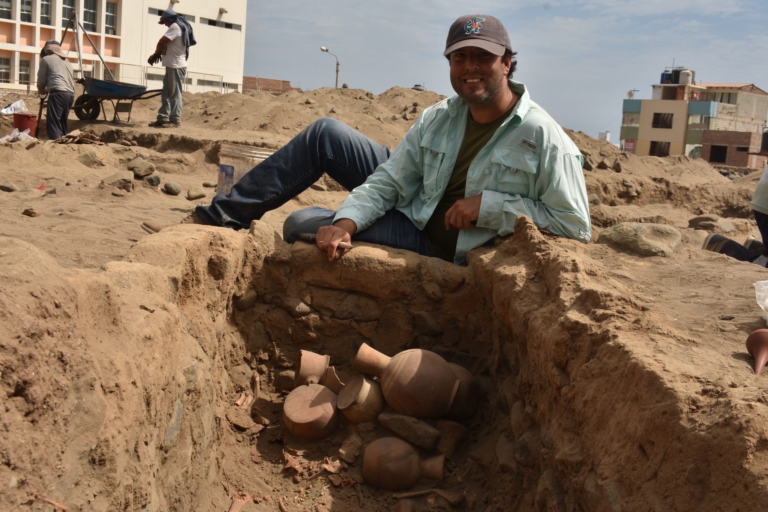Gabriel Prieto posing with some unearthed pottery fragments, which are piled in a small hole in the ground. 