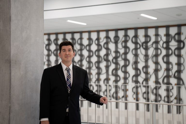 a man in a suit stands in front of an art installation of computer wires