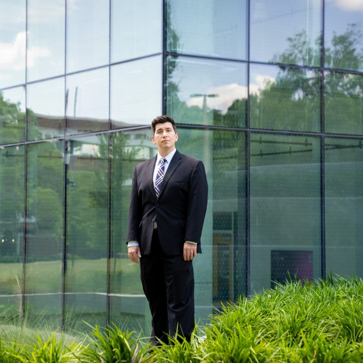 a man in a suit stands in front of a glass facade with landscaping around it