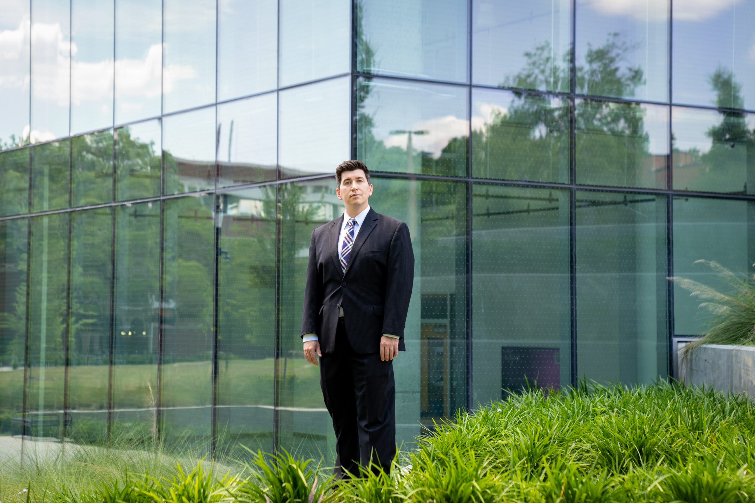 a man in a suit stands in front of a glass facade with landscaping around it